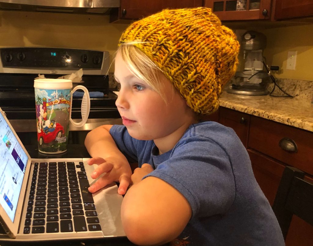 a young boy wearing an oversized, slouching Purl Swirl Hat while working on his computer