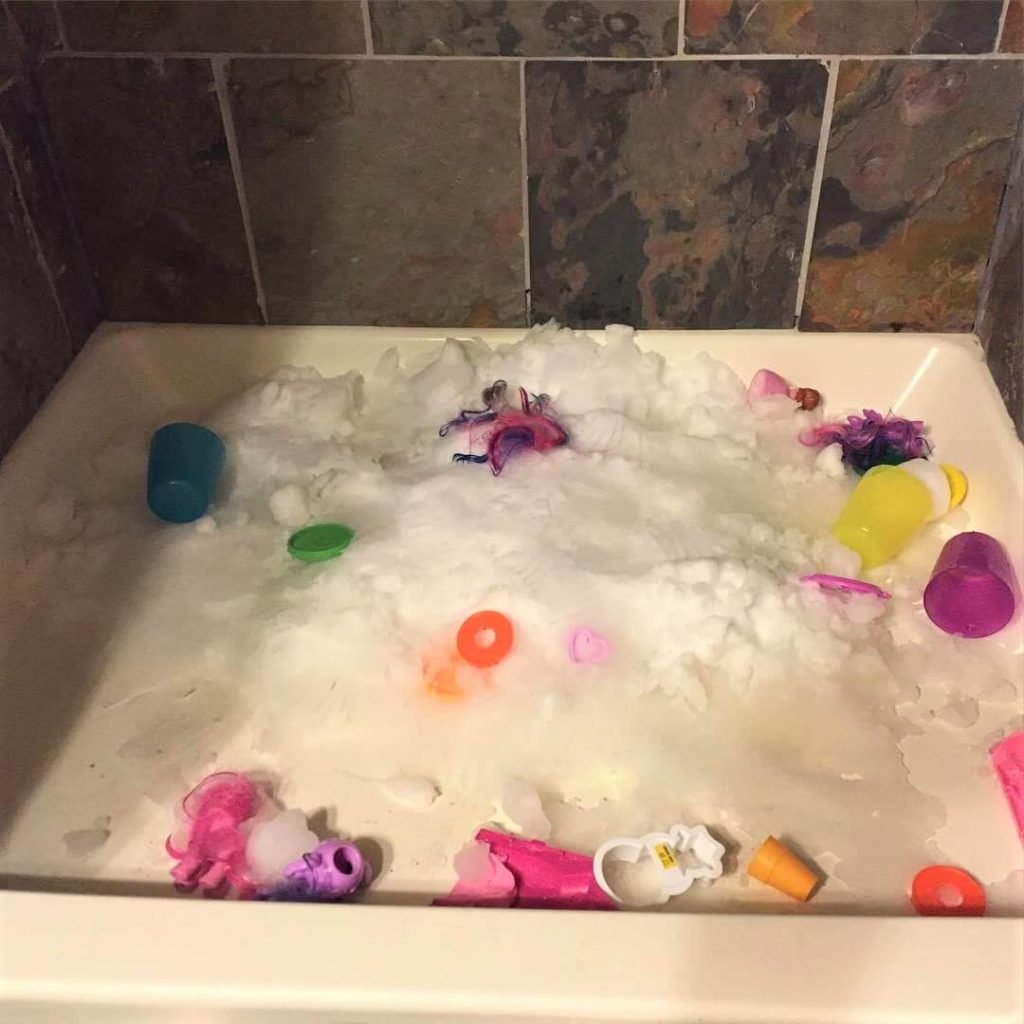 an indoor shower full of snow littered with sand toys, cups, and cookie cutters