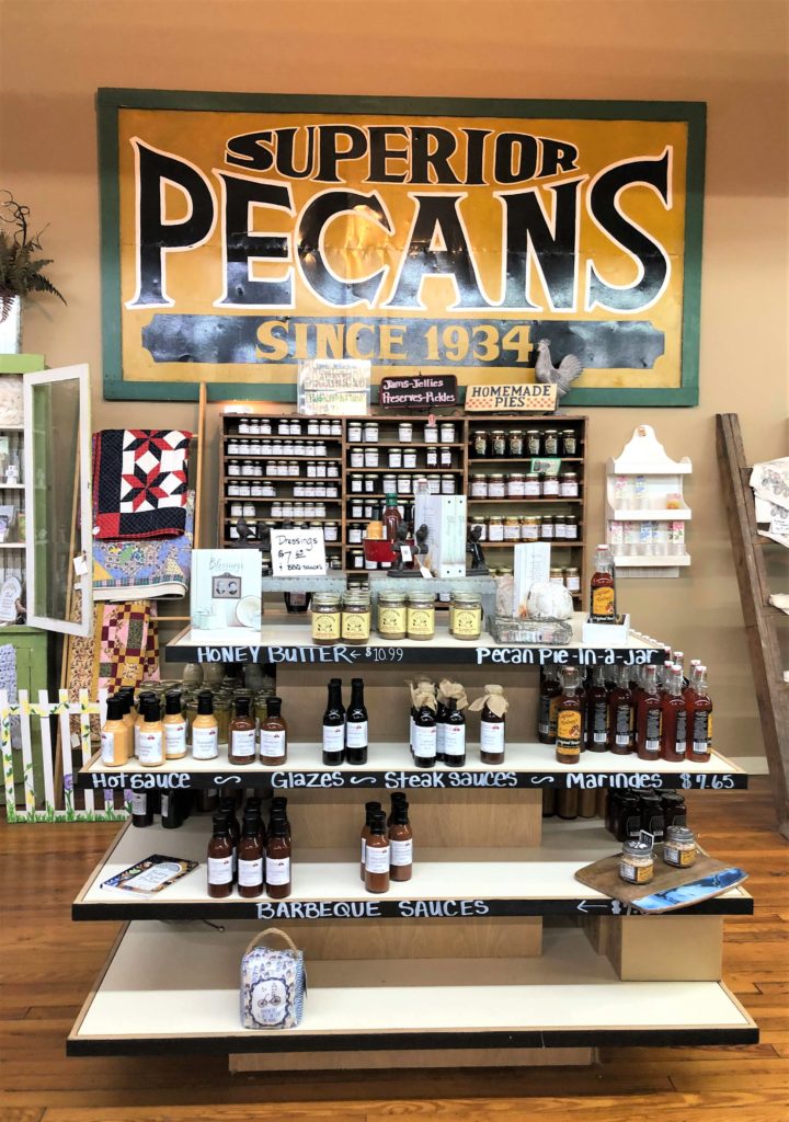 A large sign reads "Superior Pecans - Since 1934" above homemade pies, honey butter, pecan pie in a jar, hot sauce, glazes, steak sauces, marinades, and barbecue sauces