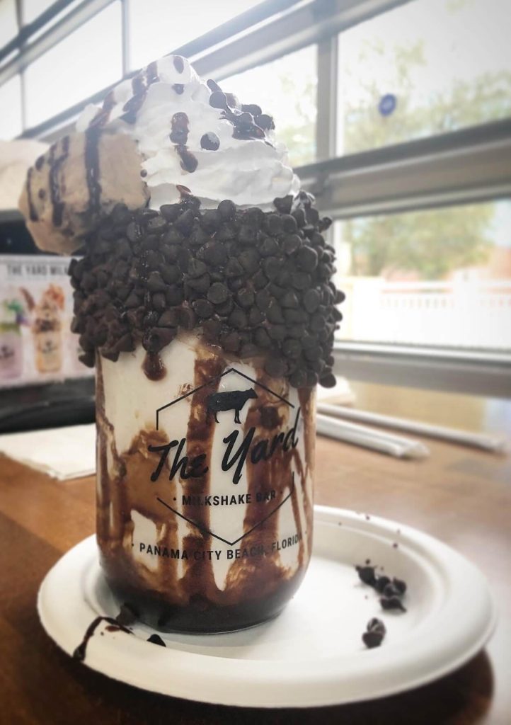 a jar of milkshake with cookie dough, whipped cream, and chocolate chips on top