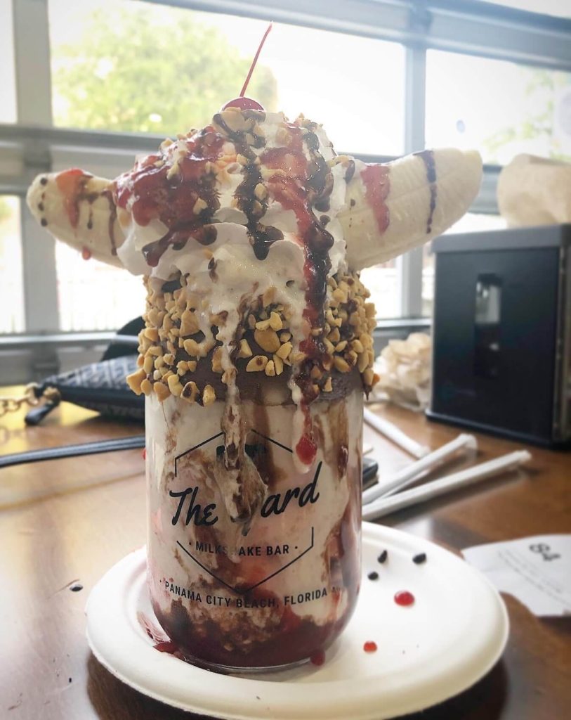 A banana carefully balanced on top of a jar full of milkshake while dropping with chocolate and strawberry sauces.
