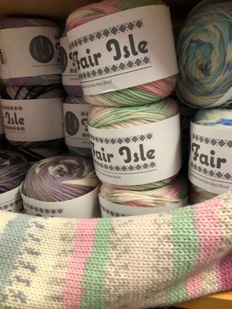 cakes of Fair Isle yarn by EYB Yarn are stacked behind a finished sample scarf knitted from the same yarn