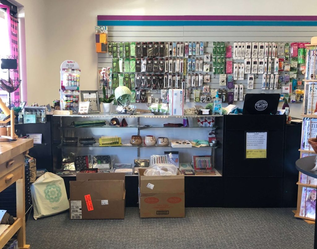 the checkout area of a yarn shop with needles, hooks, and notions hanging behind the counter