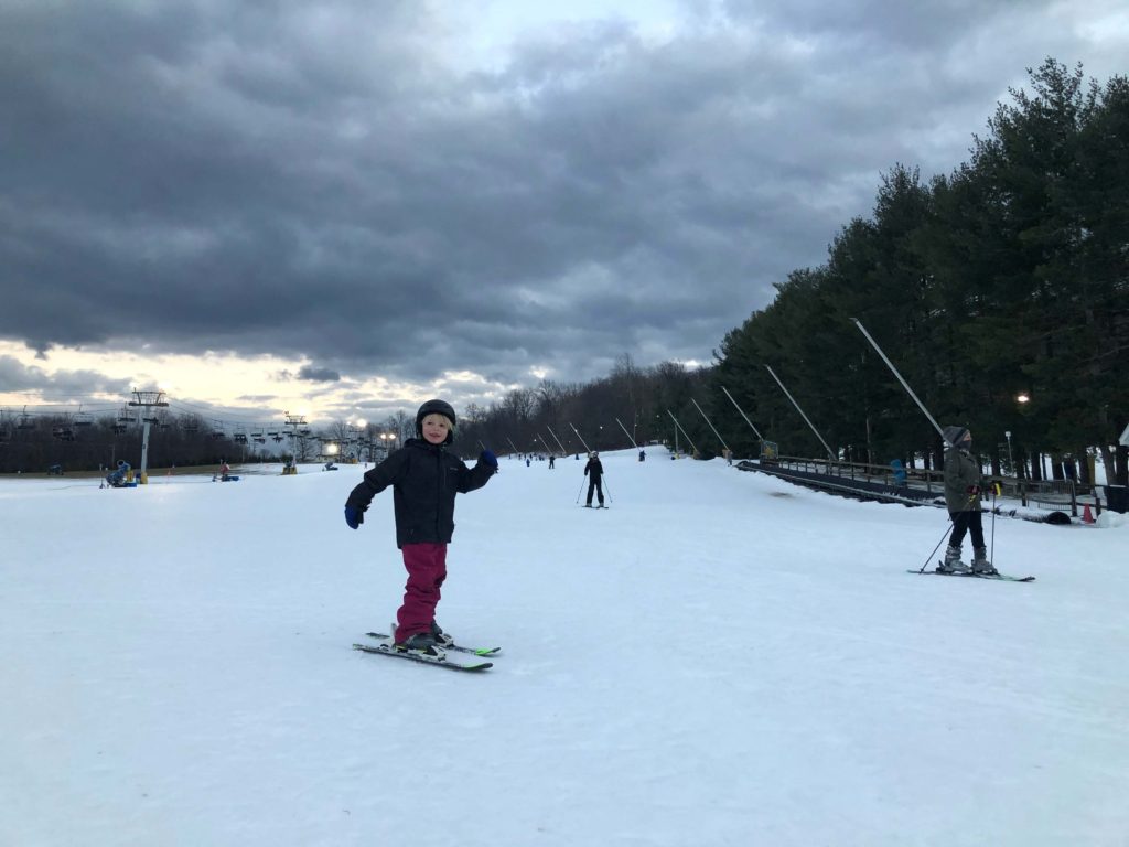 a child skis down a snow-covered slope with a ski lift behind him