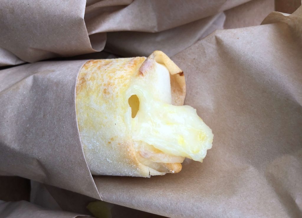 cream cheese and pineapple ooze out of a paper-wrapped spring roll