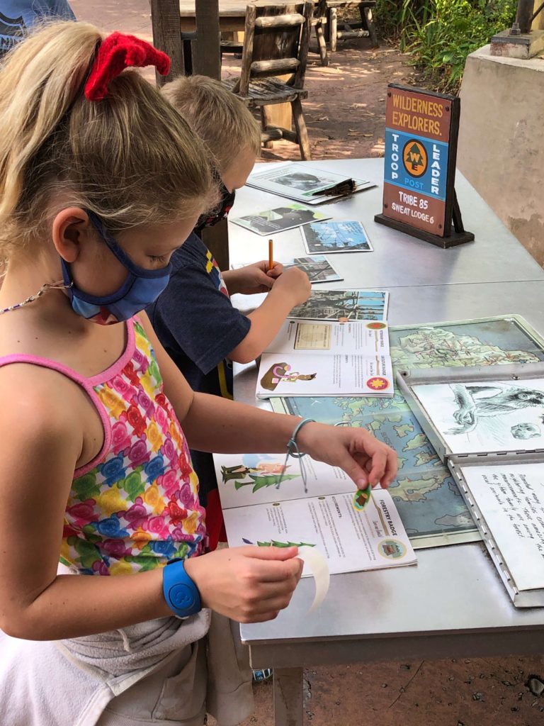 two children take notes and place badges in their Wilderness Explorer handbooks