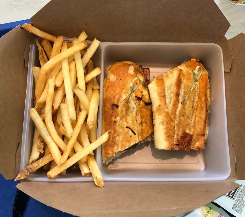 an open to-go container with a Cubano sandwich, cut in half, and French fries