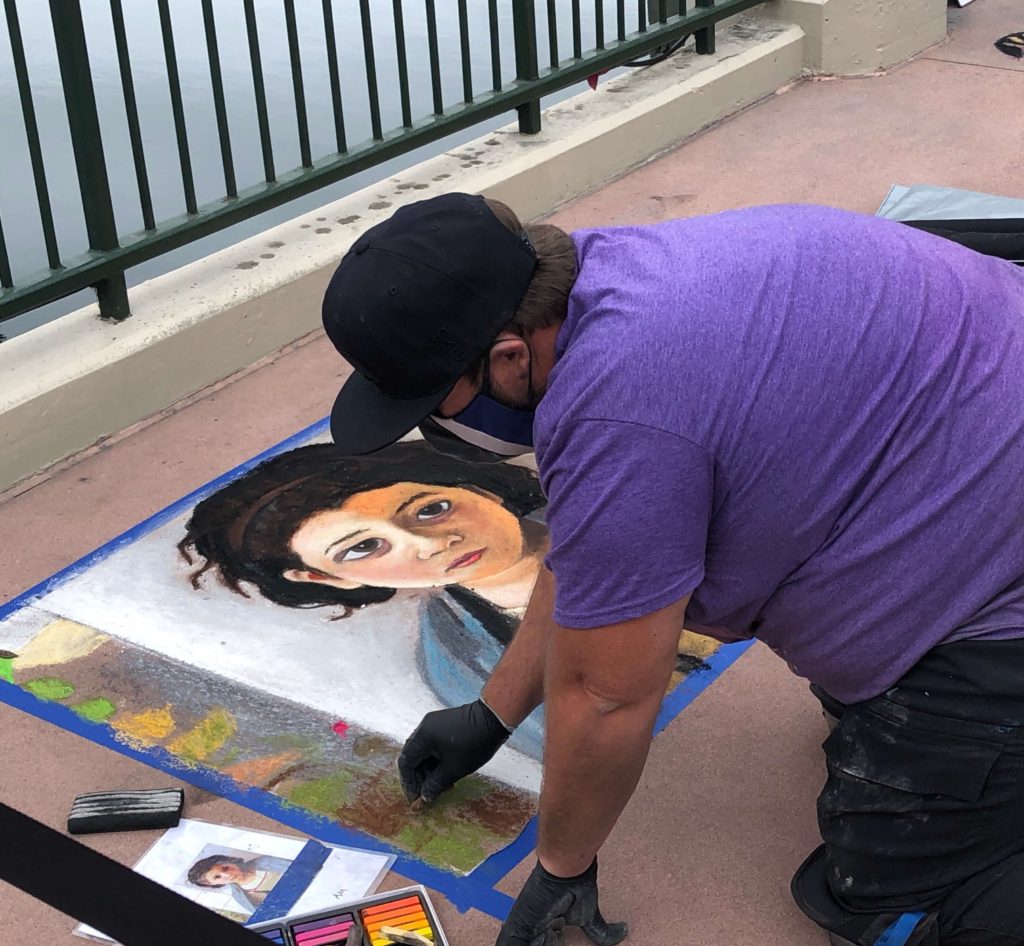 an artist uses a photo of a woman as a reference while working on the sidewalk in chalk