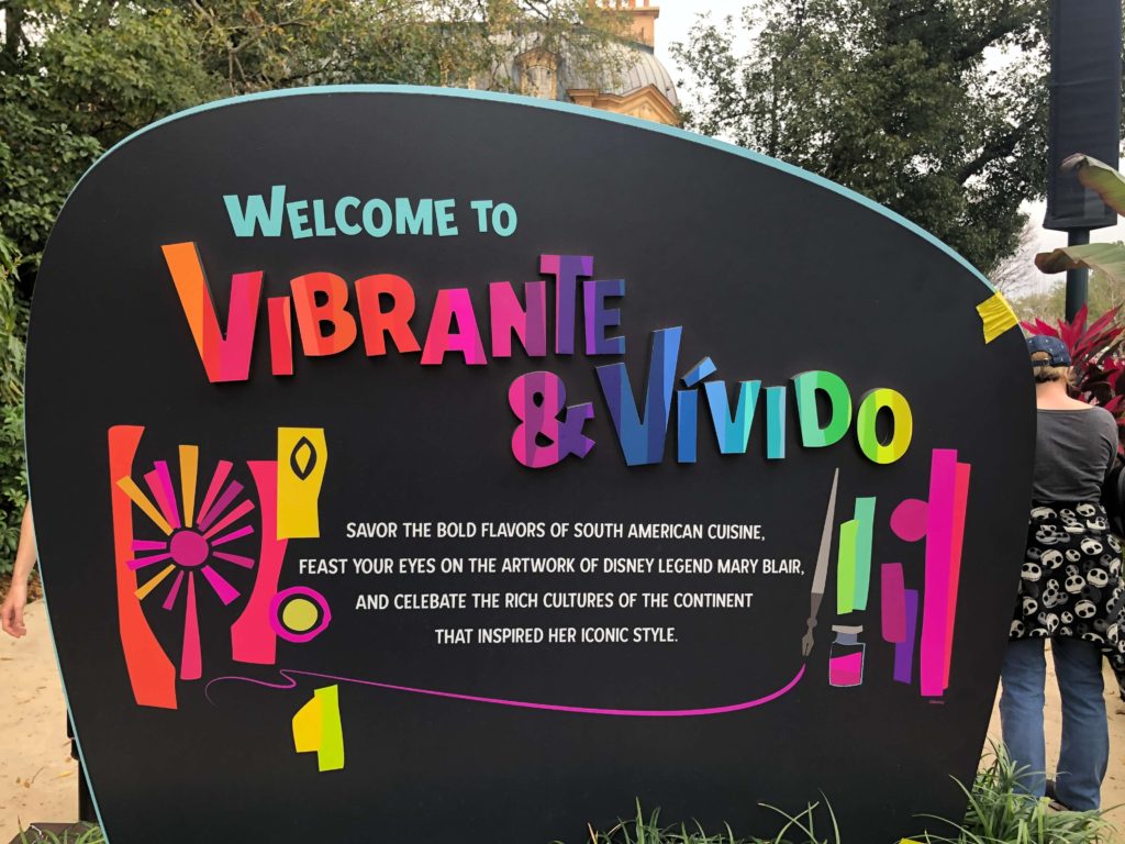 A sign reads Vibrante & Vivido Savor the bold flavors of South American cuisine, feast your eyes on the artwork of Disney Legend Mary Blair, and celebrate the rich cultures of the continent that inspired her iconic style.