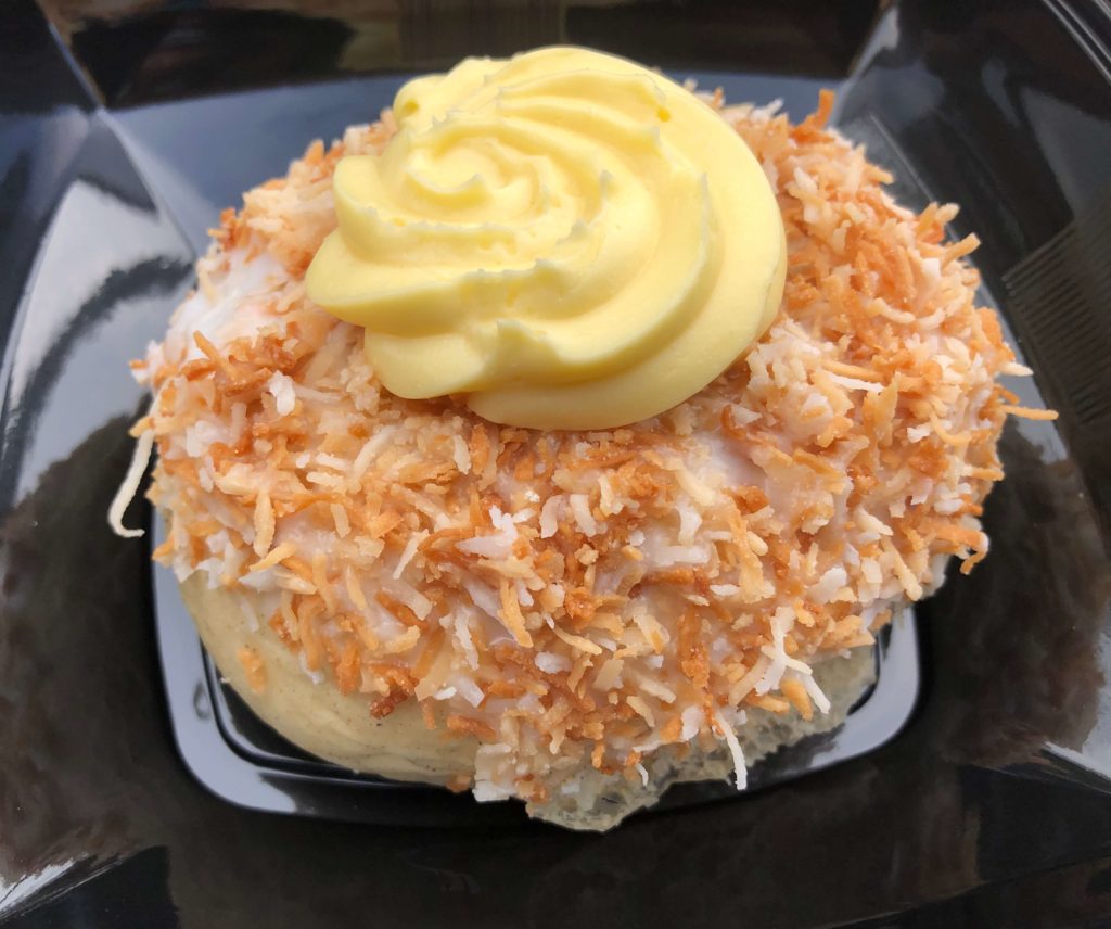 a large roll covered in coconut with a dollop of custard on top