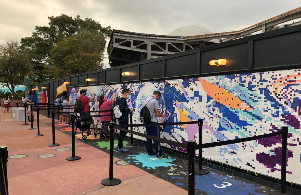 painters work on a giant paint-by-number mosaic lines a wall at Epcot