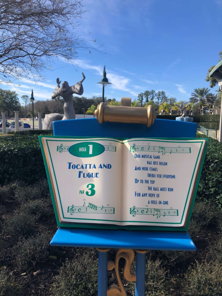 an open songbook introduces the first hole of Fantasia Gardens mini golf with this rhyme:
Our musical game has just begun
And here comes treble for everyone
Up to the top the ball must run
For any hope of a hole-in-one