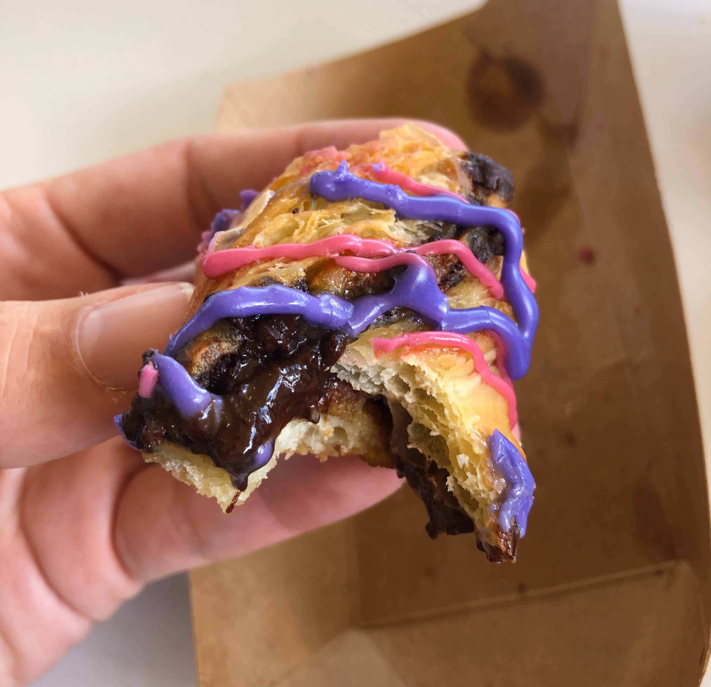 a close-up of chocolate oozing out of a puff pastry covered with pink and purple icing 