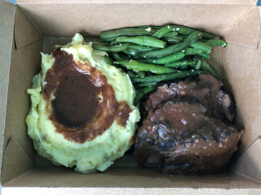 a close-up of mashed potatoes and pot roast with gravy and seasoned garlic green beans