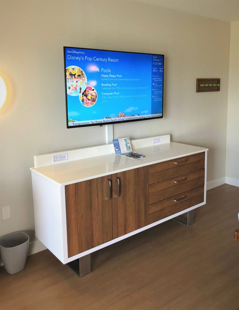 a large wall-mounted TV reads "Disney's Pop Century Resort" and lists the pool amenities