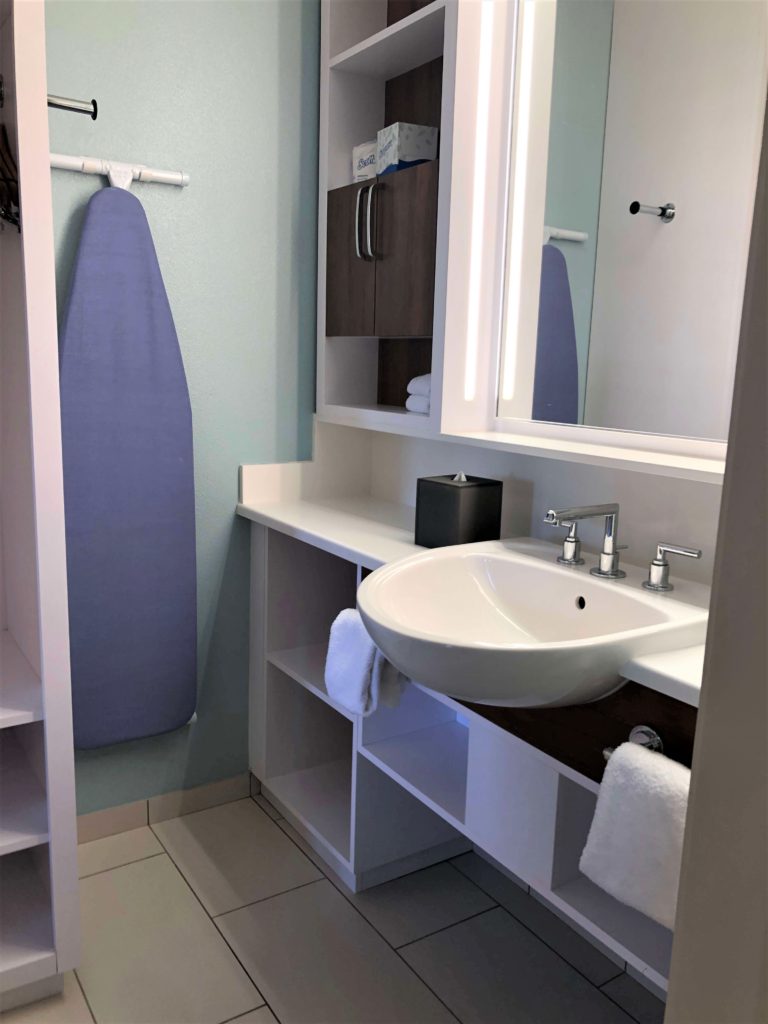 an ironing board hangs in a bathroom with many cubbies and a single sink