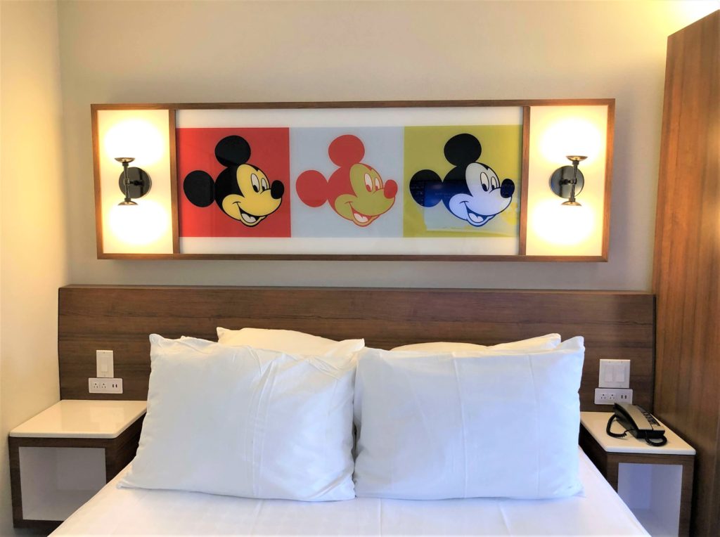 three Warhol-style pop art images of Mickey Mouse above a queen-sized bed