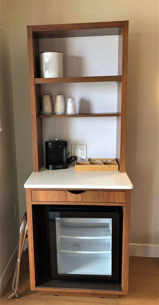 a drink station with ice bucket, single use cups, coffee maker, tea bags and coffee, and a small refrigerator