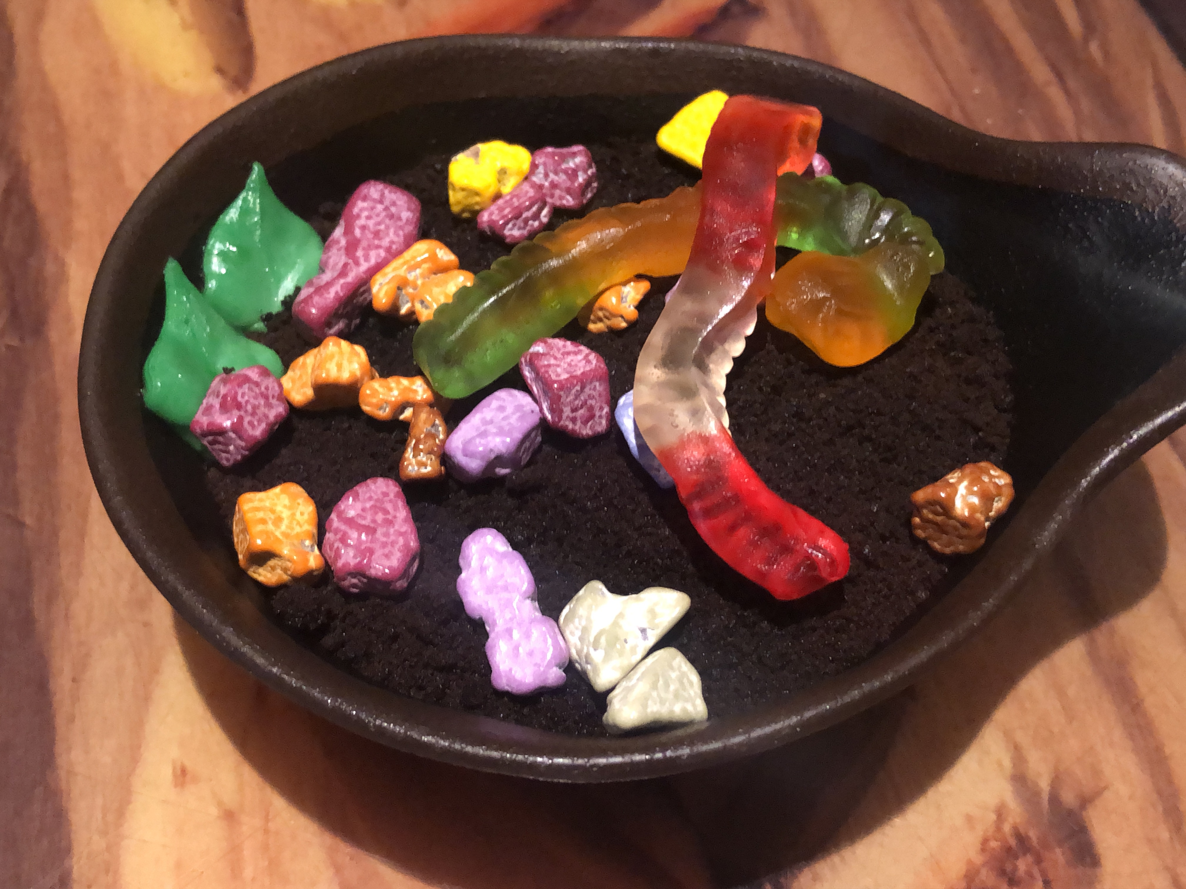 chocolate rocks, gummi worms,and  frosting leaves on a dessert covered in a bed of crushed chocolate cookies