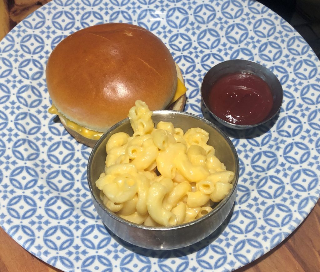 a cheeseburger, metal bowl of macaroni and cheese, and small ramekin of ketchup on a patterned plate