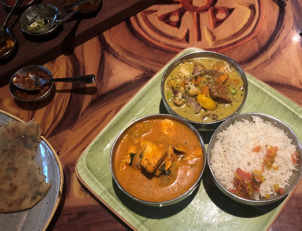 three metal bowls atop a square plate hold seafood curry and rice