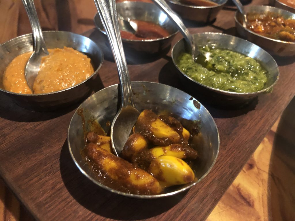 nine different sauces in small metal ramekins with matching small spoons