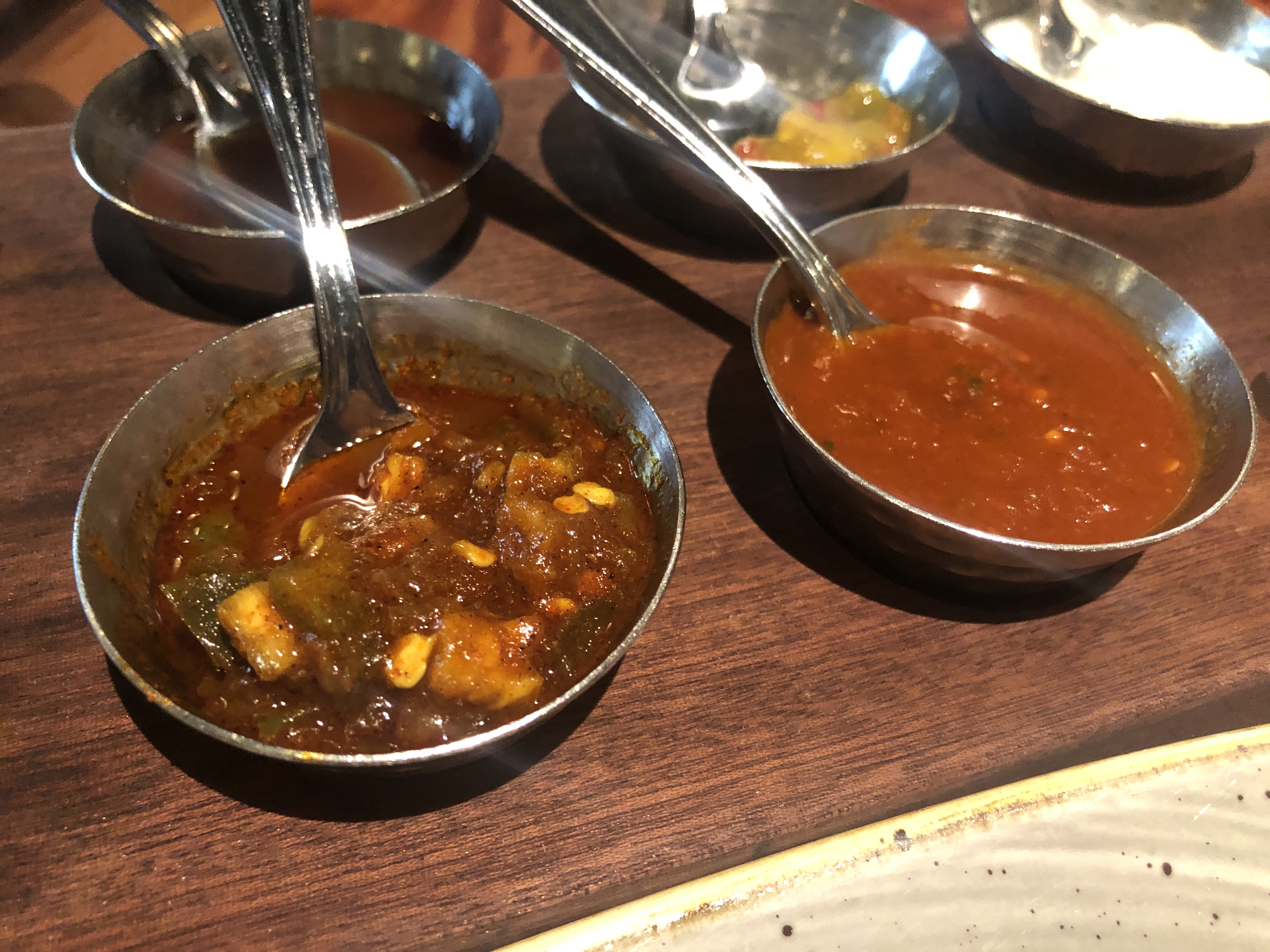nine different sauces in small metal ramekins with matching small spoons