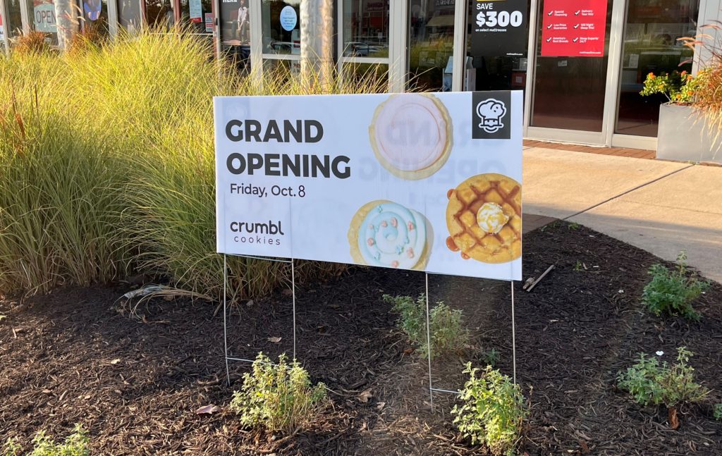 a sign announcing the grand opening of Crumbl Cookies shop on Friday, October 8