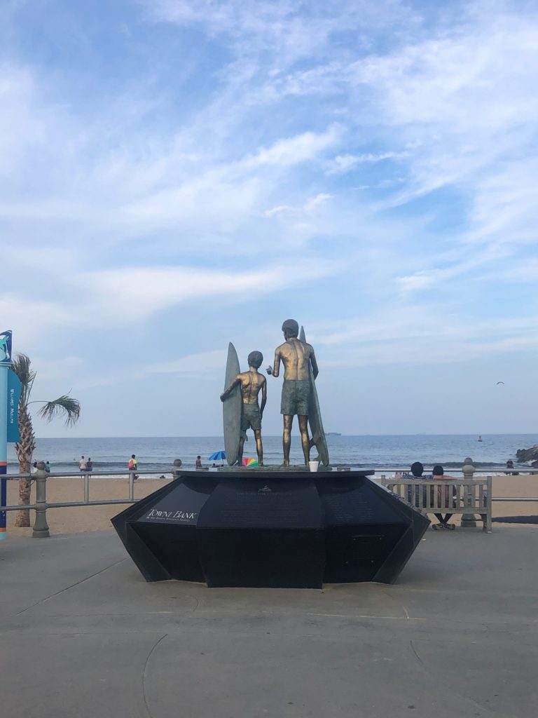 a statue of two surfers gazing out over the ocean with their boards tucked under their arms at Grommet Island on the Virginia Beach oceanfront