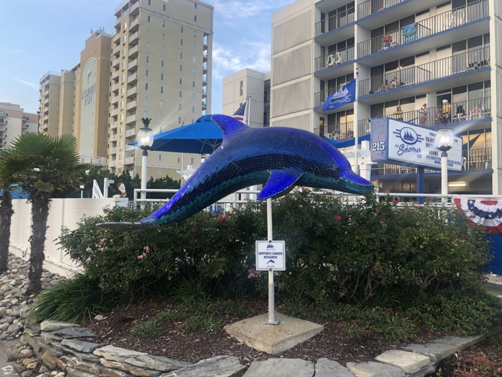 a shimmering blue Promise Dolphin statue outside of Schooners at Virginia Beach
