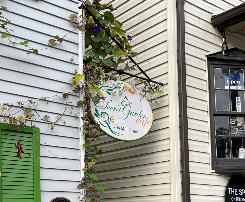 a sign for The Secret Garden Café is covered in ivy