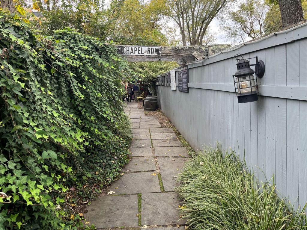 a lantern hangs on a fence and overgrown ivy moves across an already-narrow path