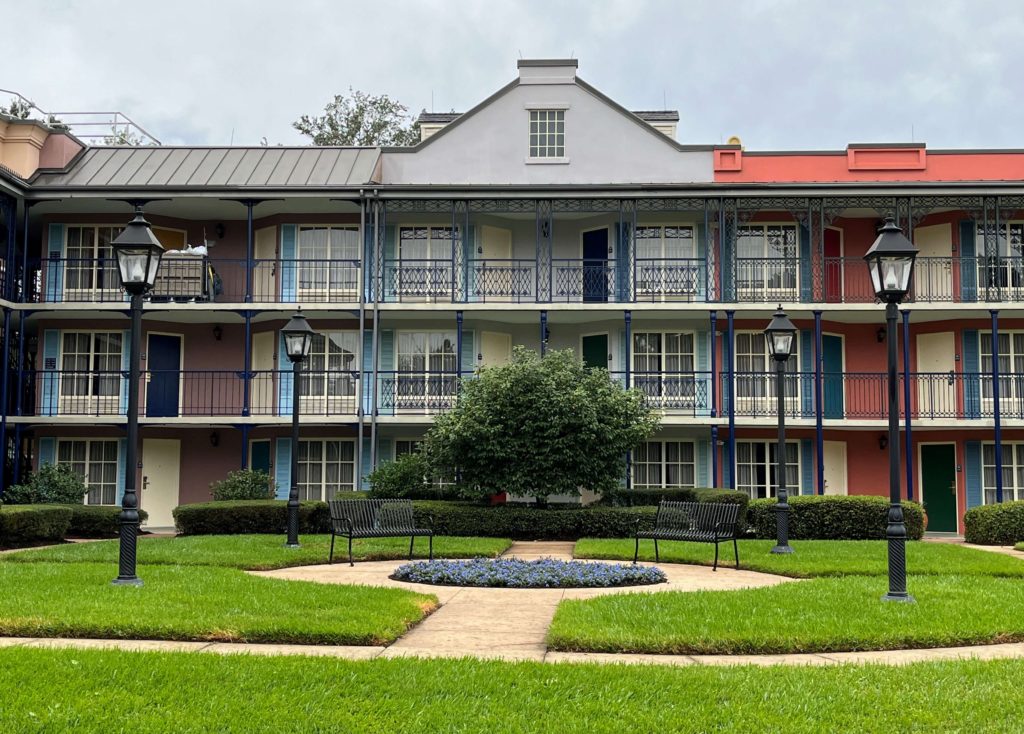 the exterior of a building at Port Orleans French Quarter features wrought iron railings, colorful paint and shutters, and parterre gardens