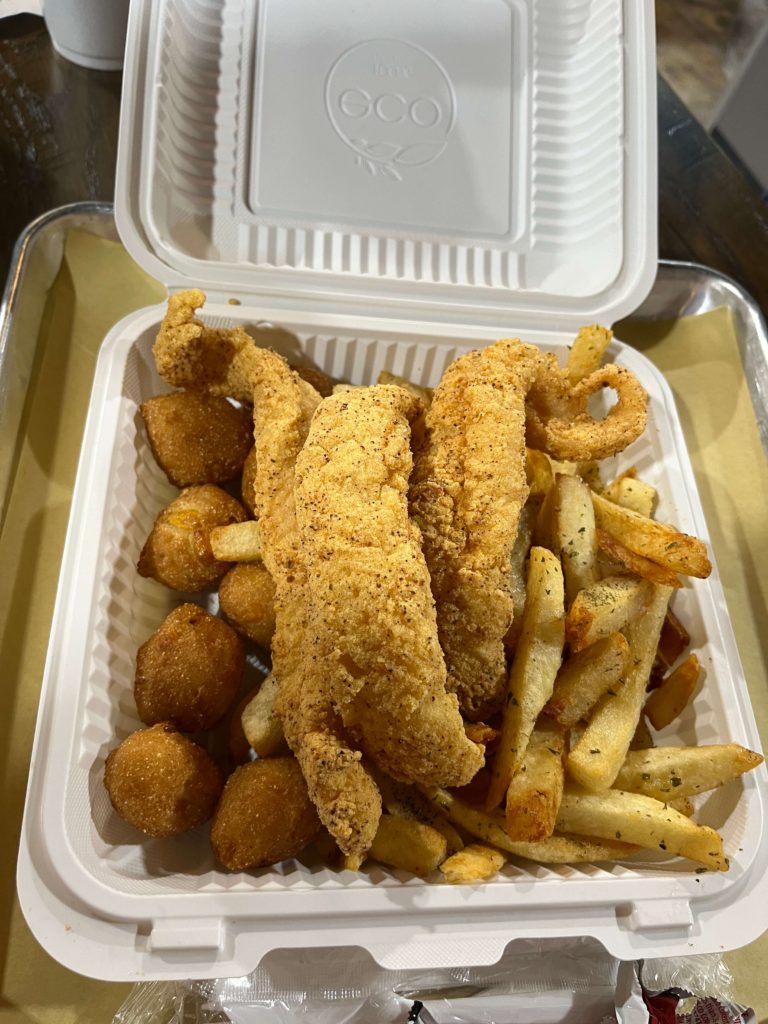 a to-go container of fish and chips with hush puppies from London Chippy at Epiq Food Hall