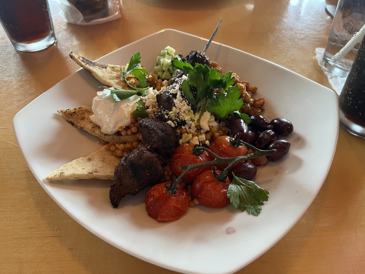 a souvlaki couscous bowl at Mythos Restaurant features cucumbers, chickpeas, beef kebab, feta, and tzatziki